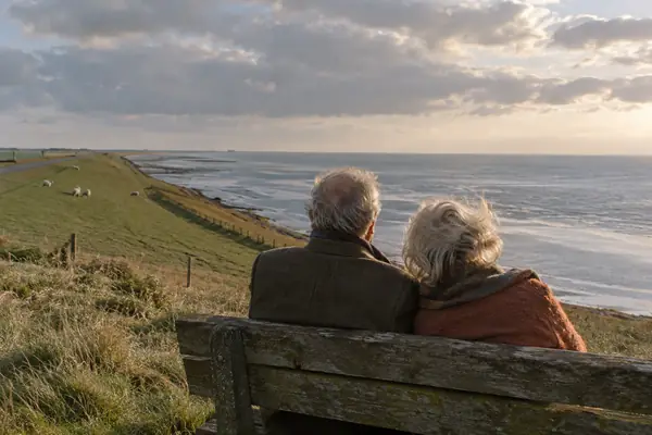 Älteres Paar von hinten auf einer Holzbank am Deich mit Blick aufs Meer